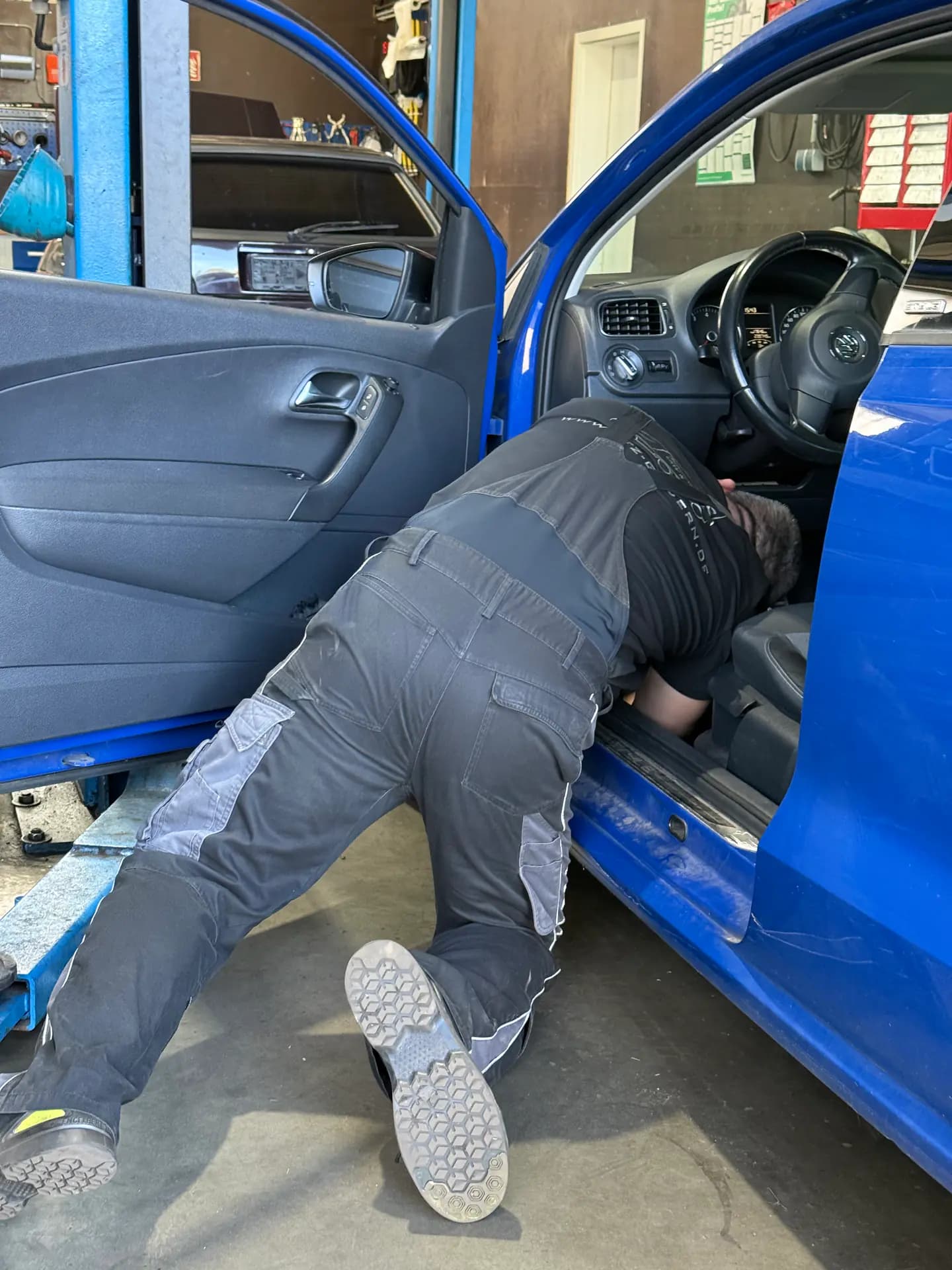 Mitarbeiter bei der Arbeit im Fußraum eines blauen Fahrzeugs