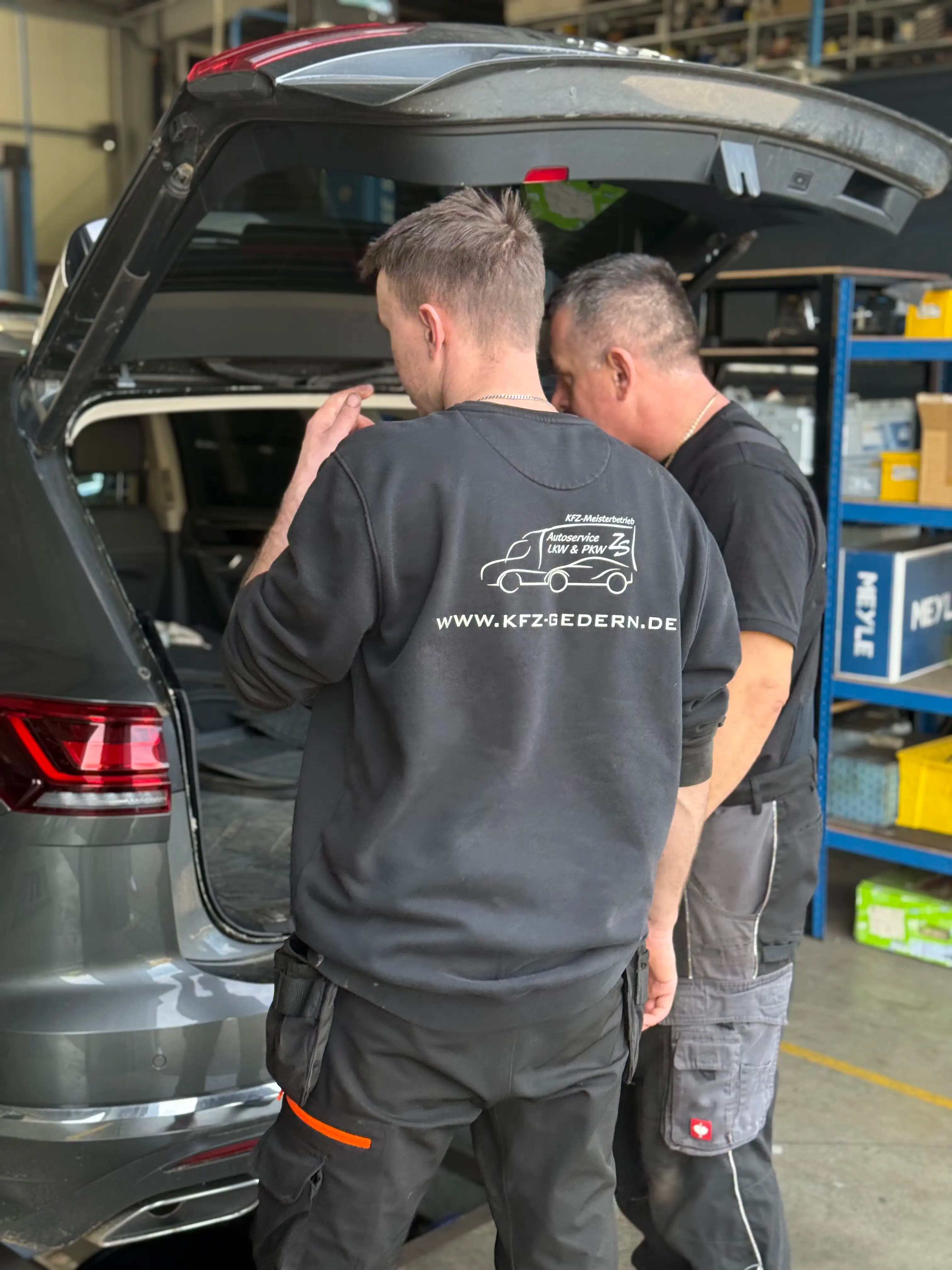 Zwei Mitarbeiter von Autoservice Suchecki bei der Arbeit am geöffneten Kofferraum eines Fahrzeugs in der Werkstatt