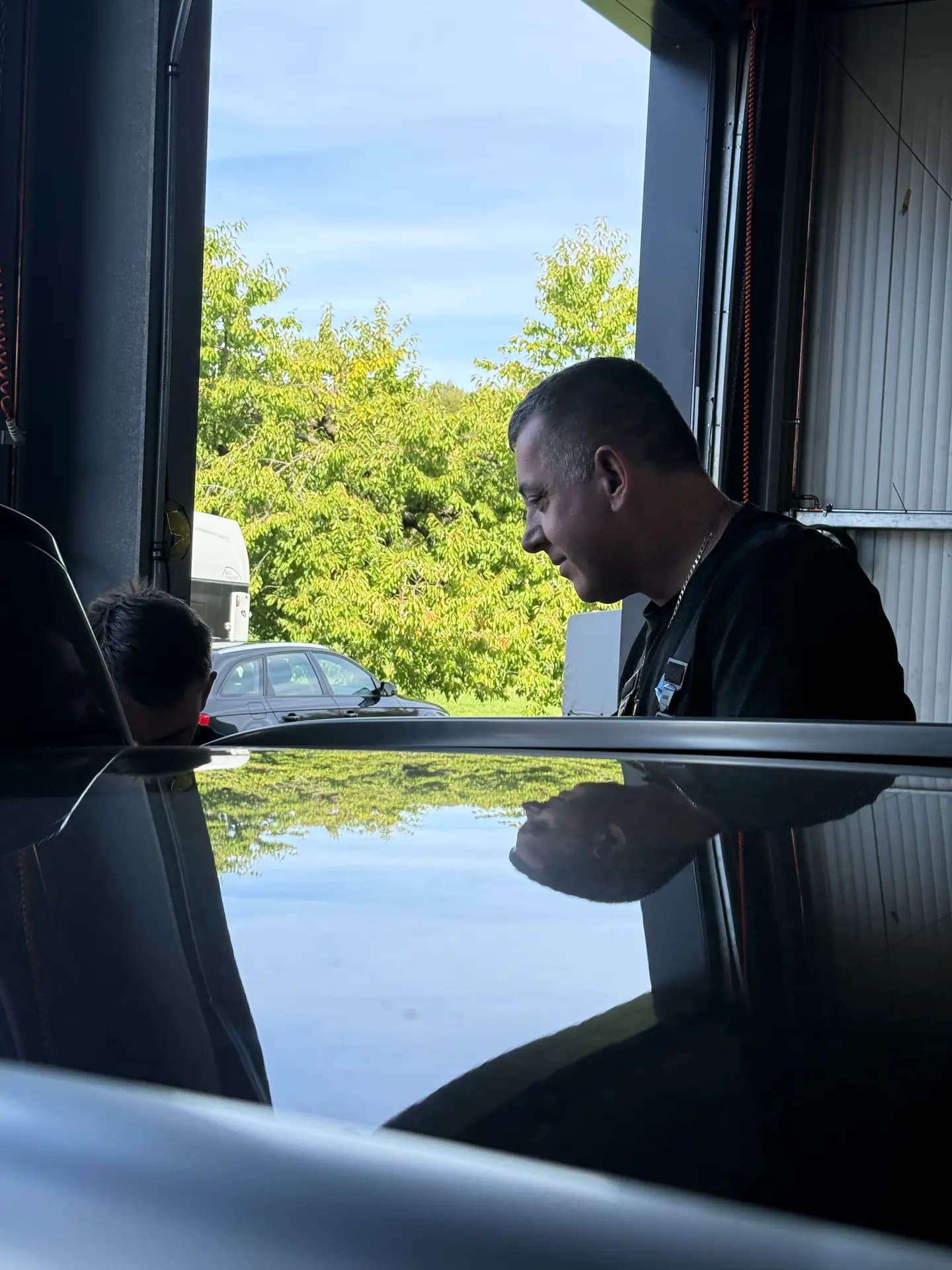 Mitarbeiter bei der Arbeit, gespiegelt im glänzenden Dach eines Fahrzeugs