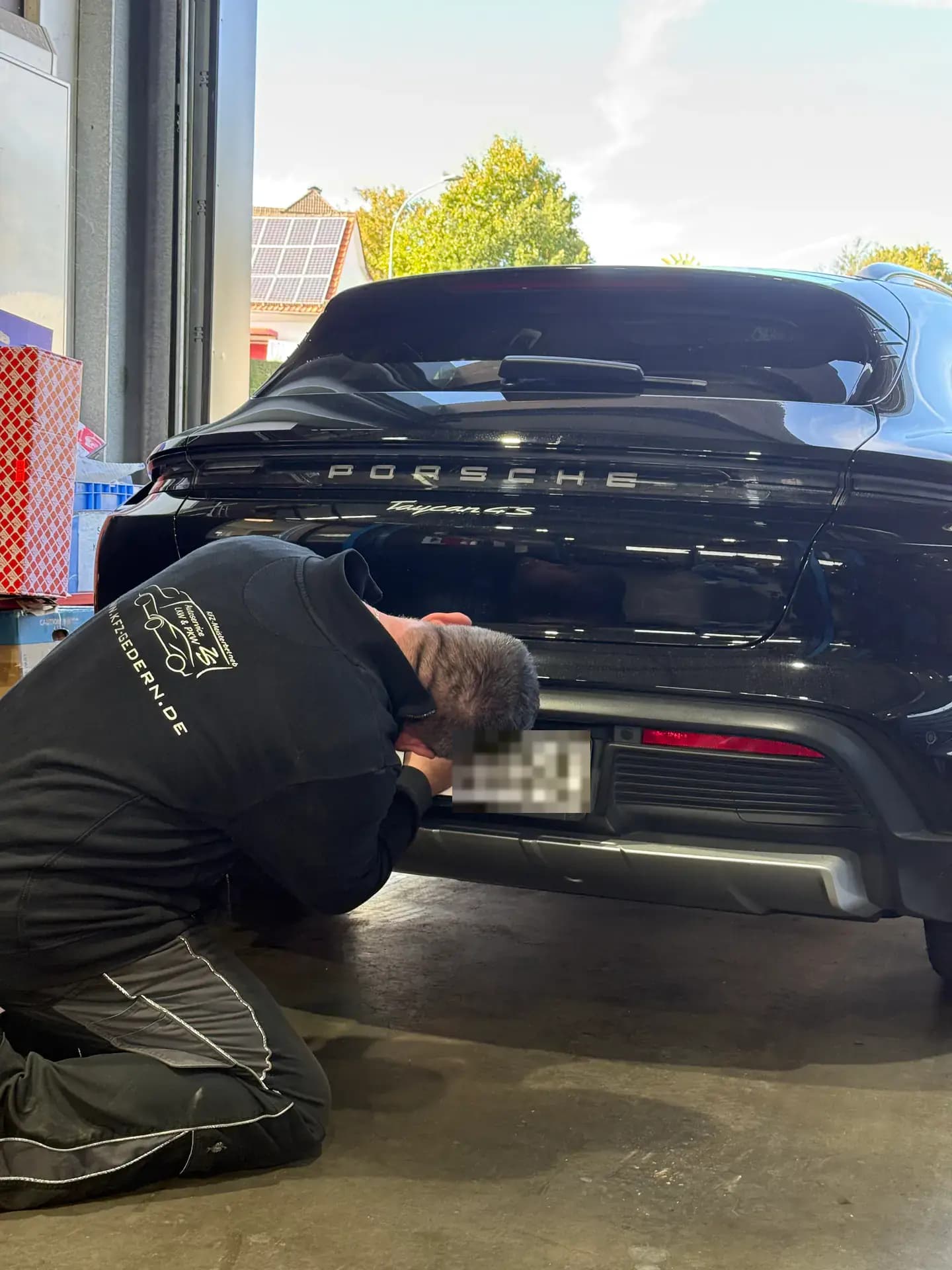 Mechaniker kniet am Heck eines schwarzen Porsche in der Werkstatt